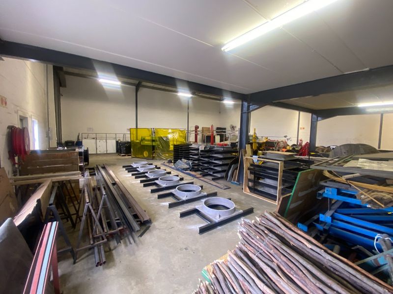 Spacious industrial utility area featuring exposed steel structural beams, concrete flooring, and overhead fluorescent lighting, suitable for manufacturing or storage operations.
