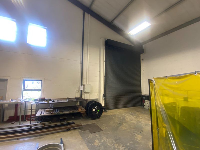 Industrial utility space featuring high ceilings, exposed steel structure, concrete flooring, and a large roller shutter door for vehicle or equipment access.