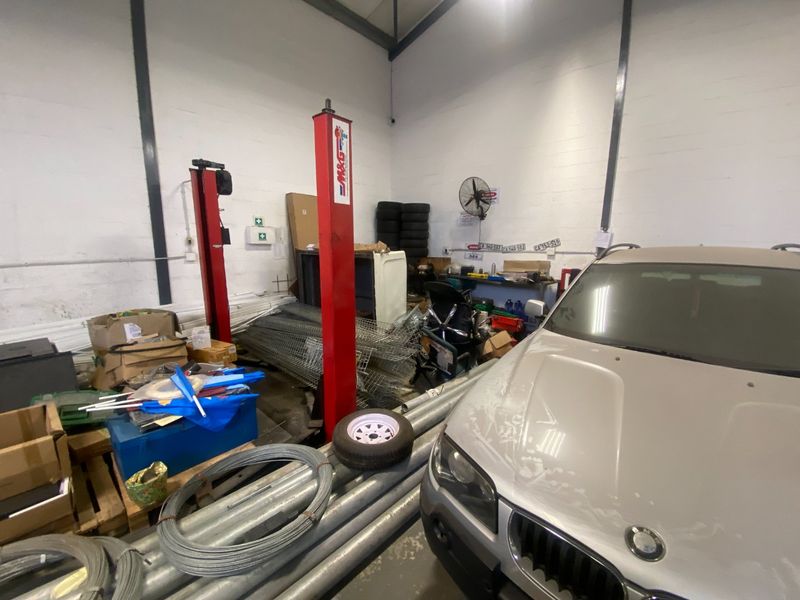 Industrial garage space featuring a two-post vehicle lift, exposed structural steel beams, and wall-mounted industrial ventilation.