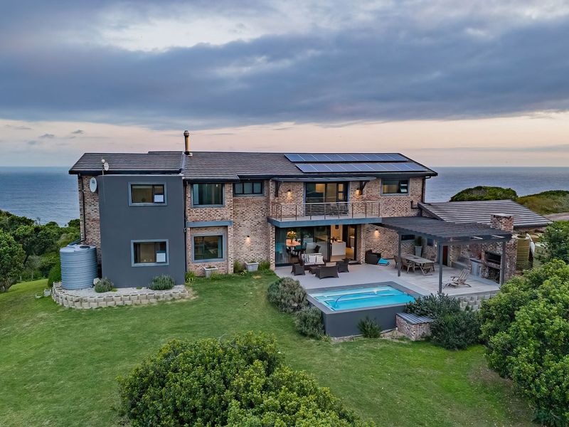 Aerial view of a modern double-story farm residence featuring a swimming pool, covered patio with built-in braai, solar panels, and expansive coastal landscape views.