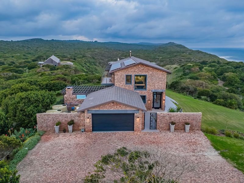 Aerial view of a modern brick farmhouse featuring a double garage, solar panels, and expansive coastal landscape views.