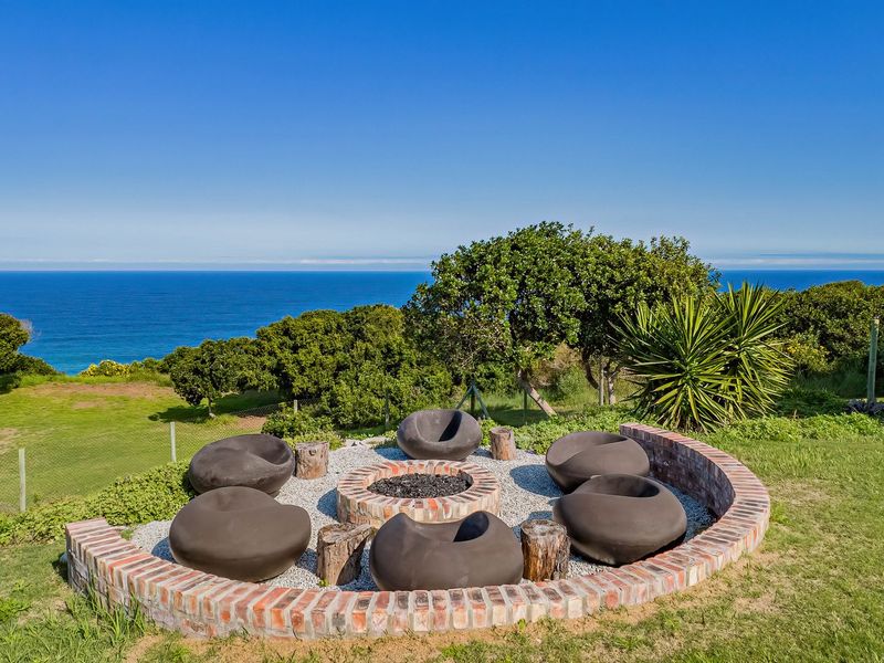 An outdoor garden area featuring a circular brick fire pit with a gravel base, set against a scenic coastal landscape.