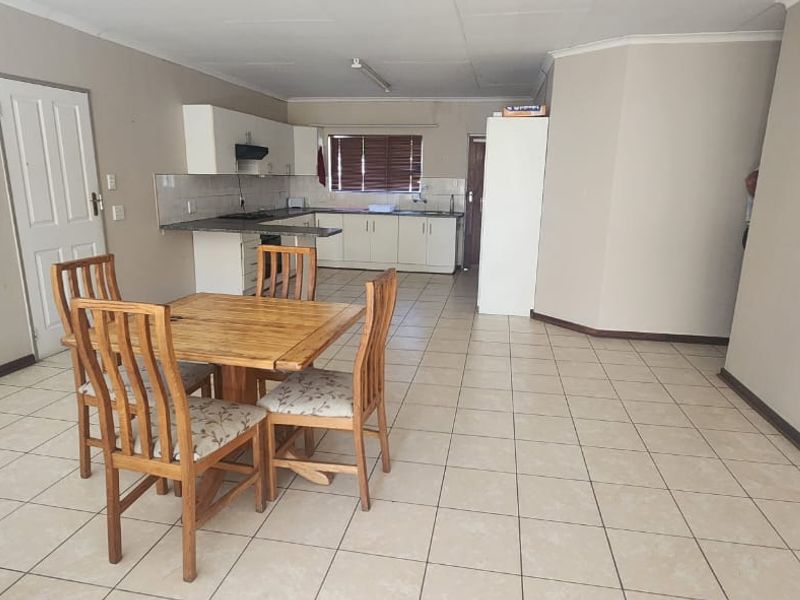 Open-plan living and kitchen area featuring tiled flooring, neutral walls, and functional built-in kitchen cabinetry with integrated appliances.