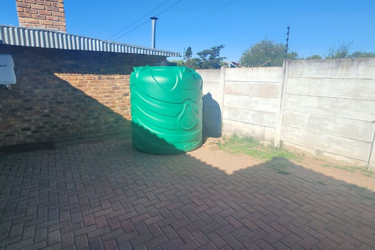 A rear exterior area featuring brick paving, a precast concrete boundary wall, and a large green water storage tank.