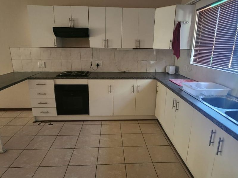Functional kitchen featuring white cabinetry, dark laminate countertops, built-in oven, gas hob, and a double bowl sink with tiled flooring and backsplash.