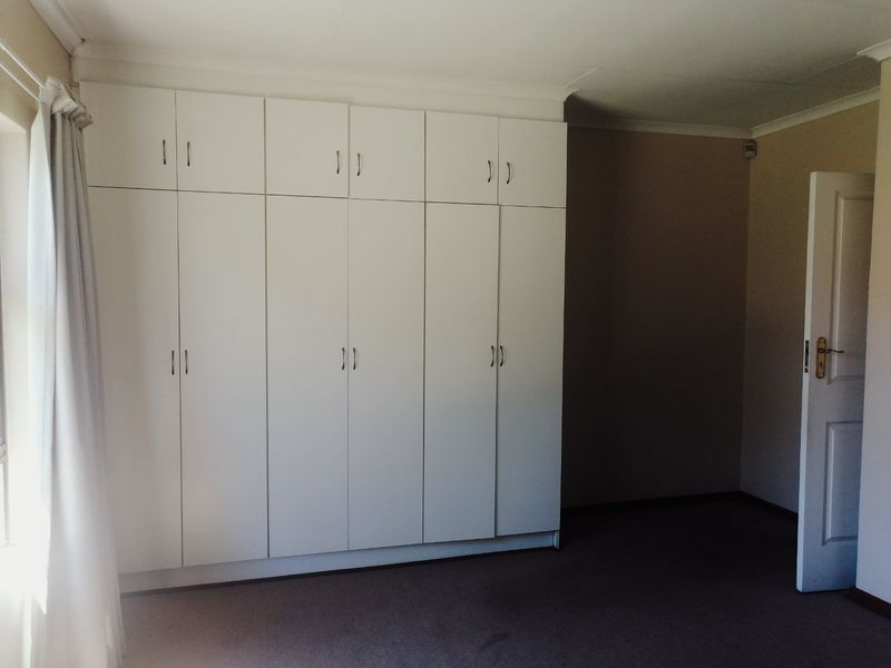 A spacious bedroom featuring extensive white built-in cupboards, neutral wall finishes, and carpeted flooring.