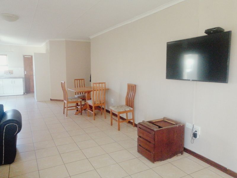 An open-plan living and dining area featuring neutral walls, tiled flooring, and a wall-mounted television, with a view toward the kitchen area.