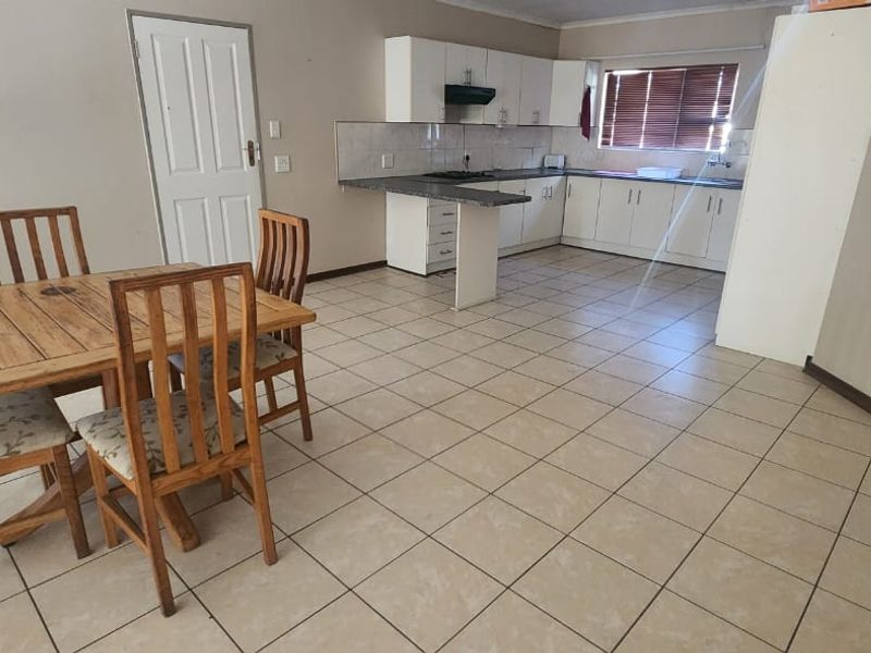 Open-plan kitchen and dining area featuring tiled flooring, white cabinetry, laminate countertops, and a functional layout with integrated hob and extractor fan.