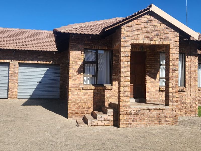A well-maintained face brick house featuring a double garage, paved driveway, and a covered entrance porch.