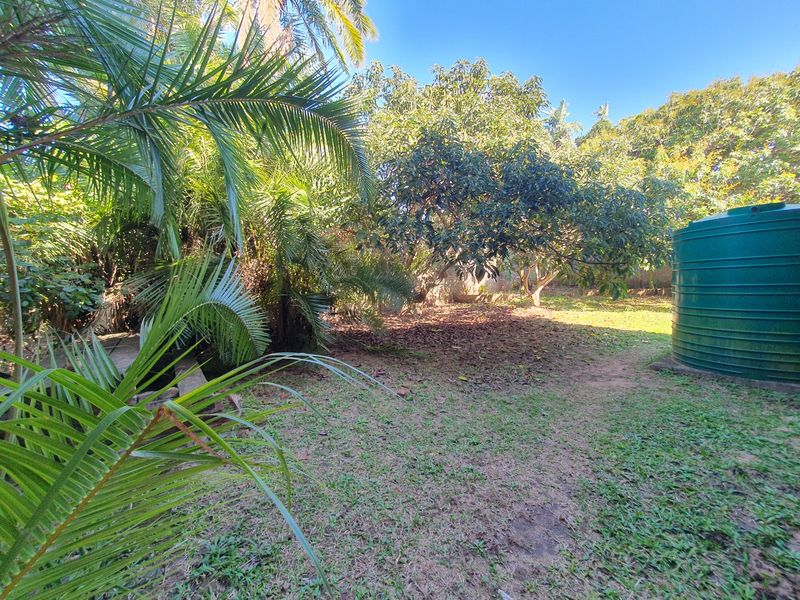 A private garden area featuring mature trees, established lawn, and a large green water storage tank.