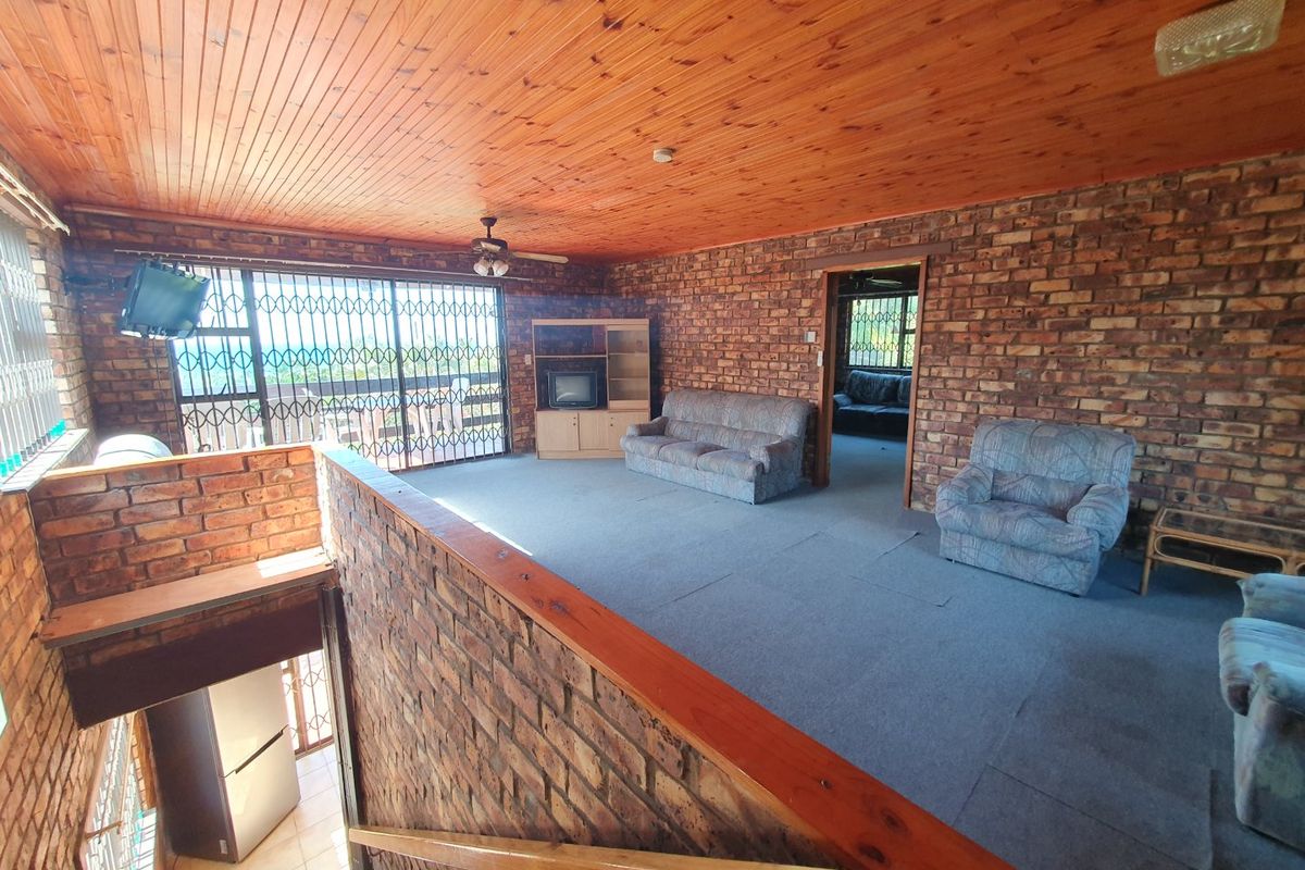 Spacious living area featuring exposed brick walls, a timber ceiling, and a staircase leading to the lower level, offering a rustic aesthetic.