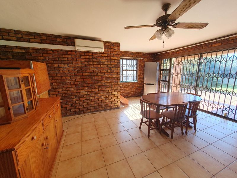 Dining area featuring exposed brick walls, ceramic floor tiles, a ceiling fan, and direct access to the garden through a sliding glass door.
