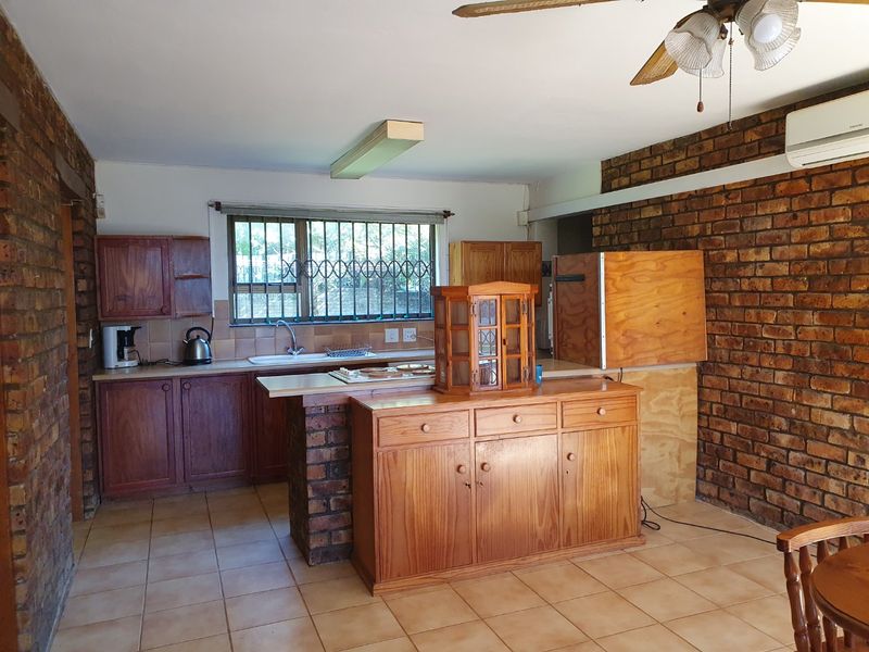Kitchen featuring exposed brick walls, tiled flooring, and wooden cabinetry with a breakfast bar and integrated sink area.