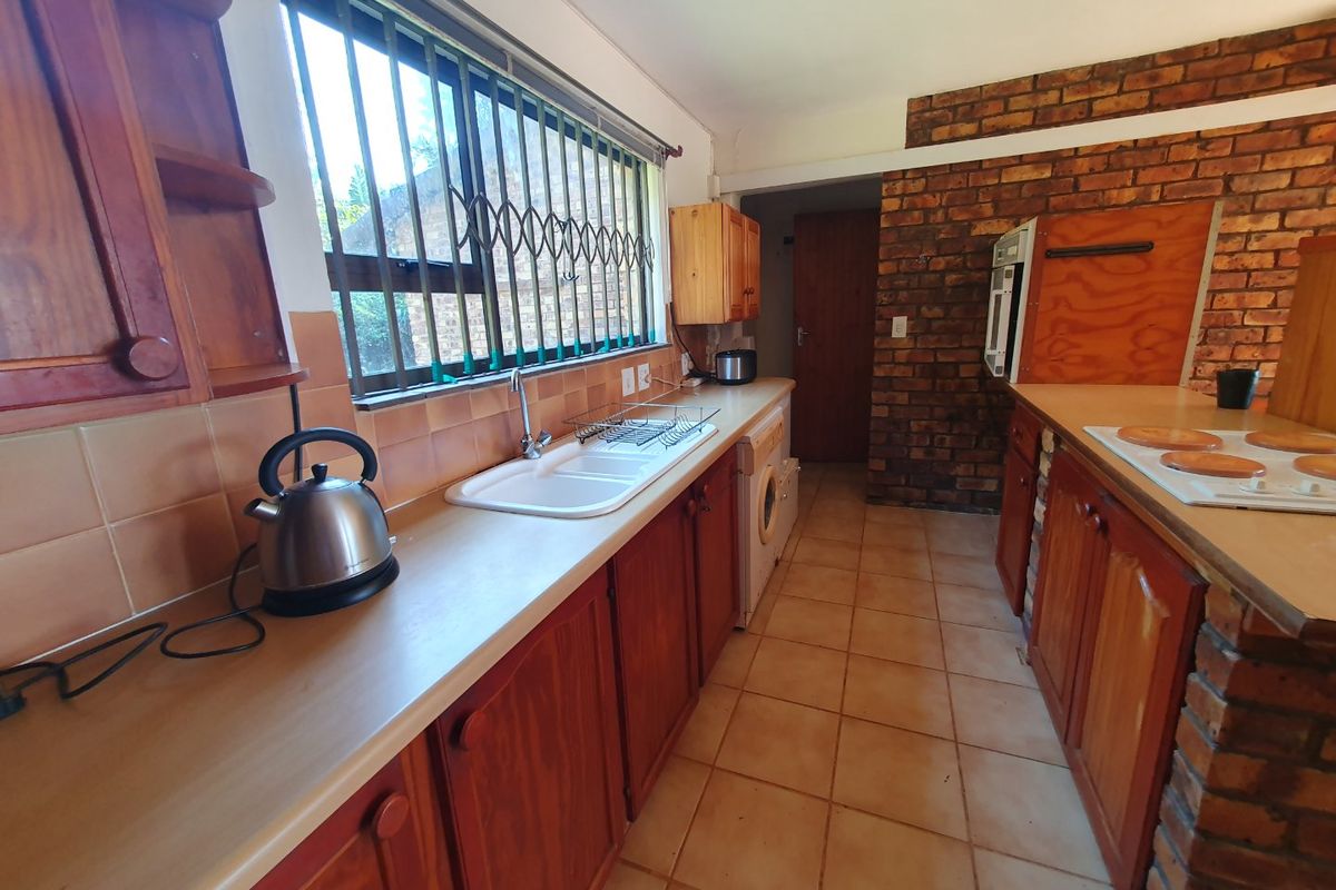 A functional kitchen featuring wooden cabinetry, laminate countertops, a double basin sink, and an exposed brick feature wall with tiled flooring.