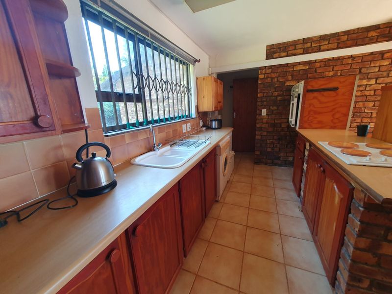 A functional kitchen featuring wooden cabinetry, laminate countertops, a double basin sink, and an exposed brick feature wall with tiled flooring.