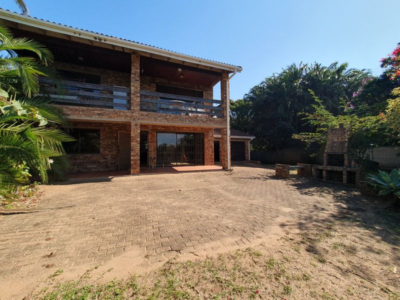 Rear view of a double-story face brick house featuring a covered patio, balcony, paved courtyard, and a built-in brick braai area.