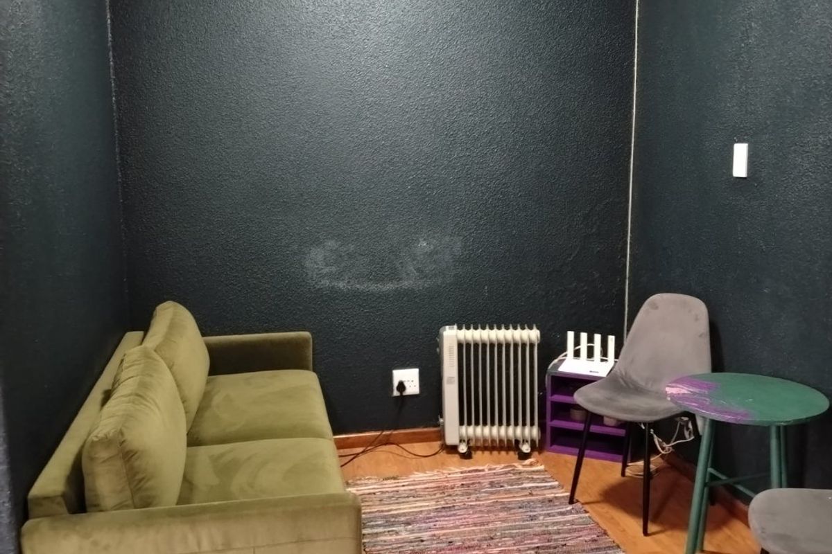 A small living area featuring dark painted walls, laminate flooring, and coving. The space requires cosmetic updates to address wall scuffs and improve overall finish.