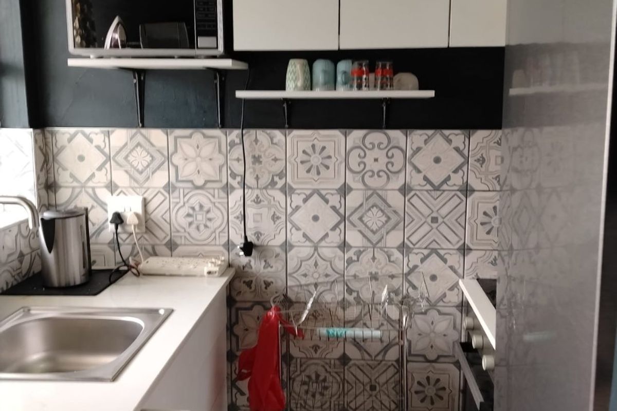 Compact kitchen featuring white cabinetry, a stainless steel sink, built-in oven, and decorative patterned tile backsplash.