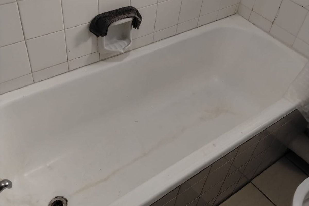 A functional bathroom featuring a built-in bathtub with ceramic wall and floor tiling, currently showing signs of wear and staining.
