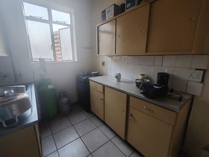 A dated kitchen featuring original cabinetry, tiled backsplash, and tiled flooring, offering significant potential for modernization and renovation.