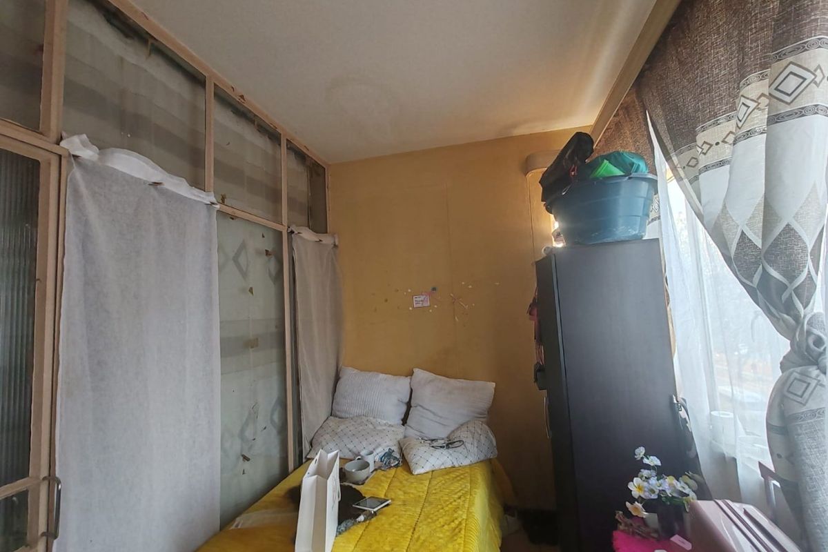 A small bedroom featuring a large window and a built-in partition wall, currently showing signs of wear and requiring cosmetic updates.
