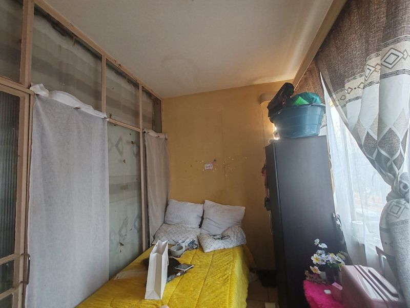 A small bedroom featuring a large window and a built-in partition wall, currently showing signs of wear and requiring cosmetic updates.