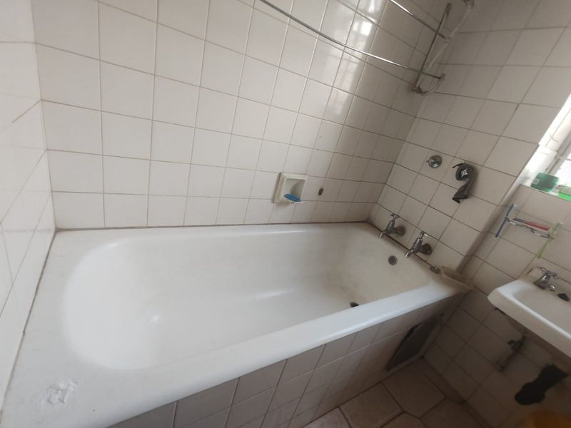 A functional bathroom featuring a built-in bathtub, wall-mounted basin, and classic white ceramic wall tiling, offering a blank canvas for modern renovation.