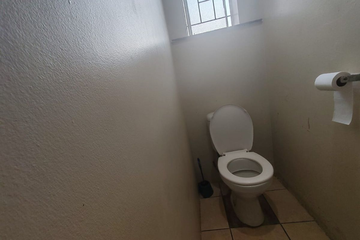 A compact, functional bathroom featuring a standard toilet, tiled flooring, and a window with security bars.