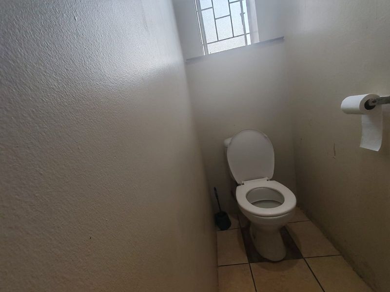 A compact, functional bathroom featuring a standard toilet, tiled flooring, and a window with security bars.