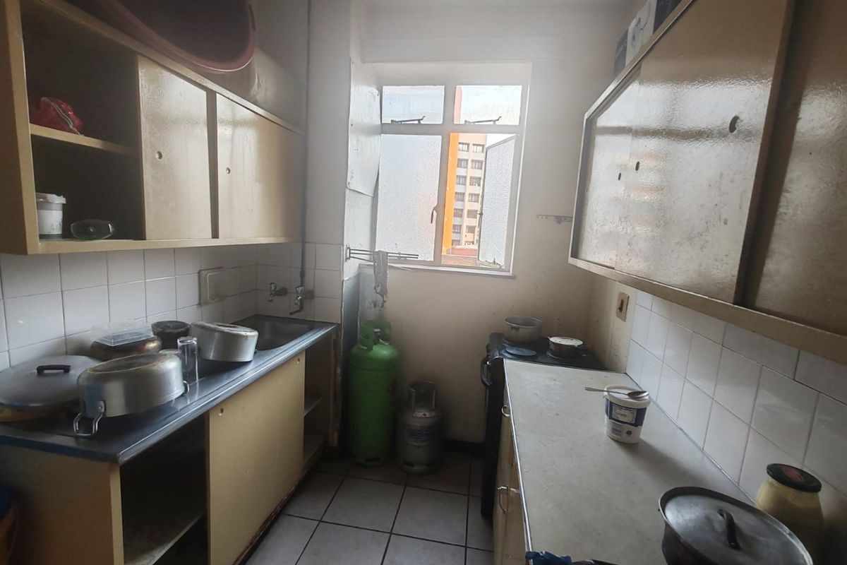 A compact kitchen featuring built-in cabinetry, a stainless steel sink, tiled backsplash, and tiled flooring, offering a functional layout in need of cosmetic updates.
