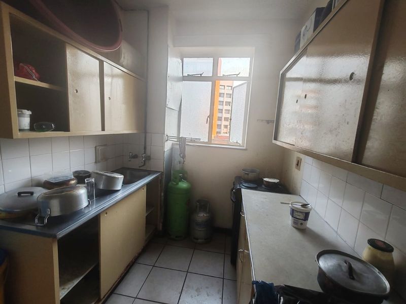 A compact kitchen featuring built-in cabinetry, a stainless steel sink, tiled backsplash, and tiled flooring, offering a functional layout in need of cosmetic updates.