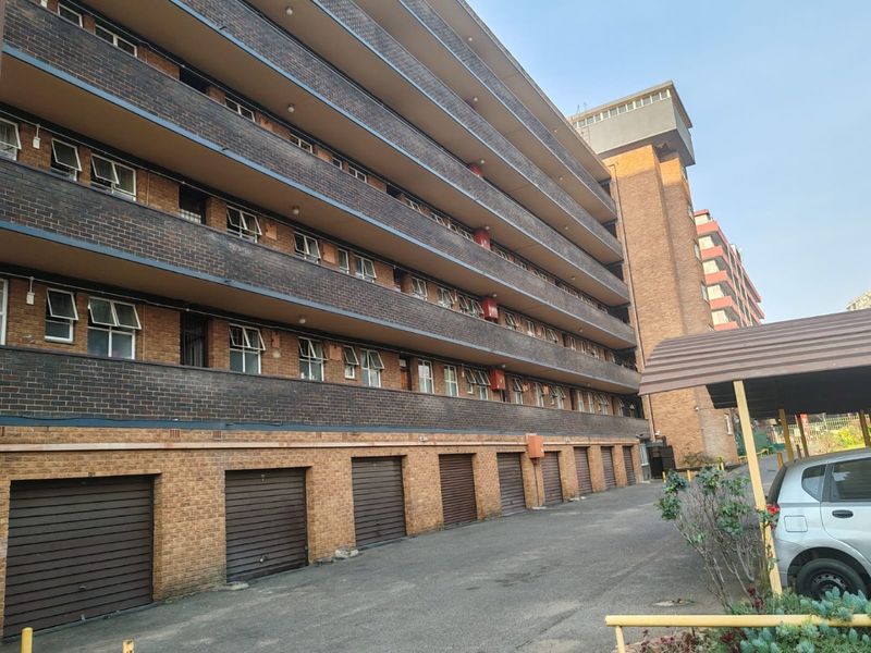 Exterior view of a multi-story apartment building featuring a brick facade, multiple ground-level garage units, and an asphalt driveway.