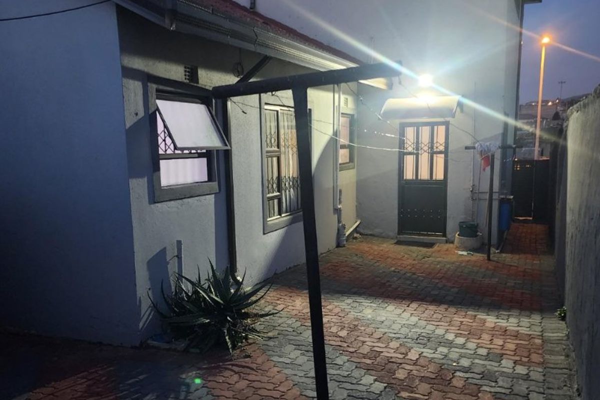 Rear exterior view of the property featuring paved courtyard area, security gates, and external lighting at dusk.