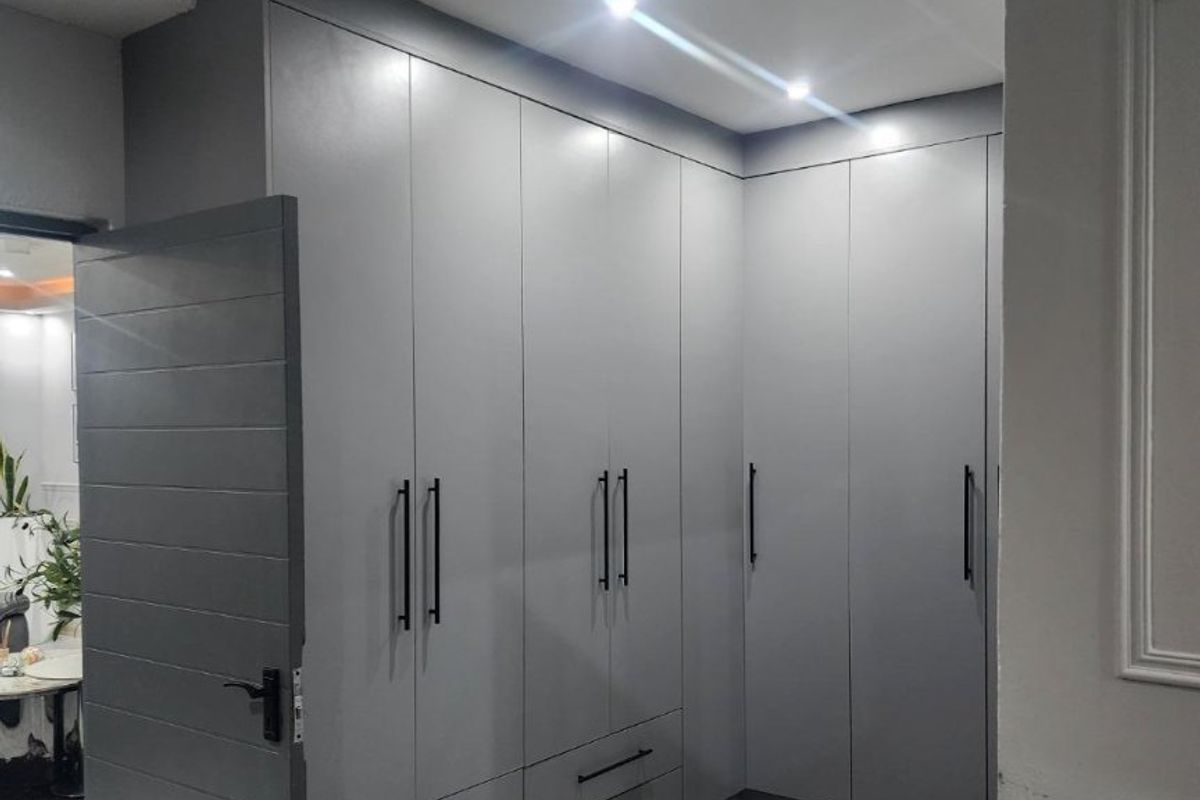 A modern bedroom featuring extensive grey built-in cupboards, recessed downlighting, and high-quality laminate flooring with decorative ceiling cornicing.