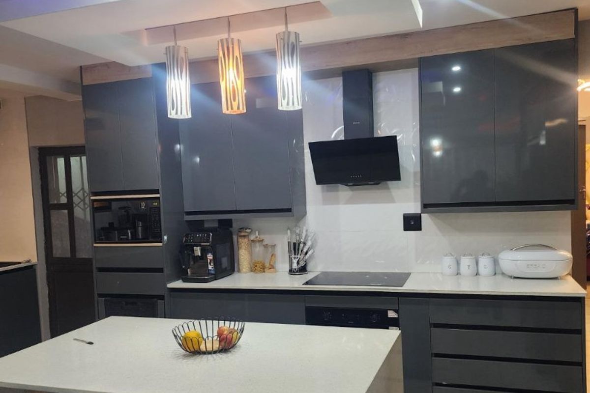 Modern kitchen featuring high-gloss grey cabinetry, stone countertops, a central island, and integrated appliances with stylish recessed ceiling lighting.