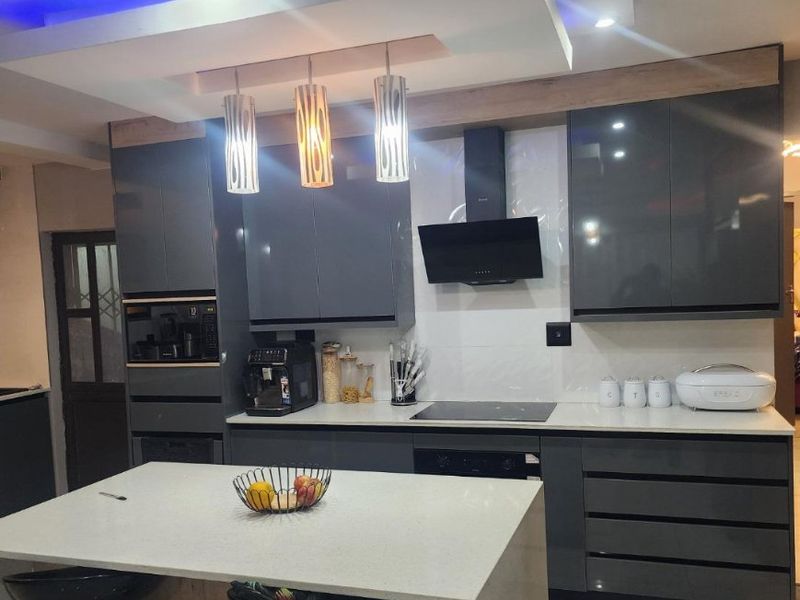 Modern kitchen featuring high-gloss grey cabinetry, stone countertops, a central island, and integrated appliances with stylish recessed ceiling lighting.