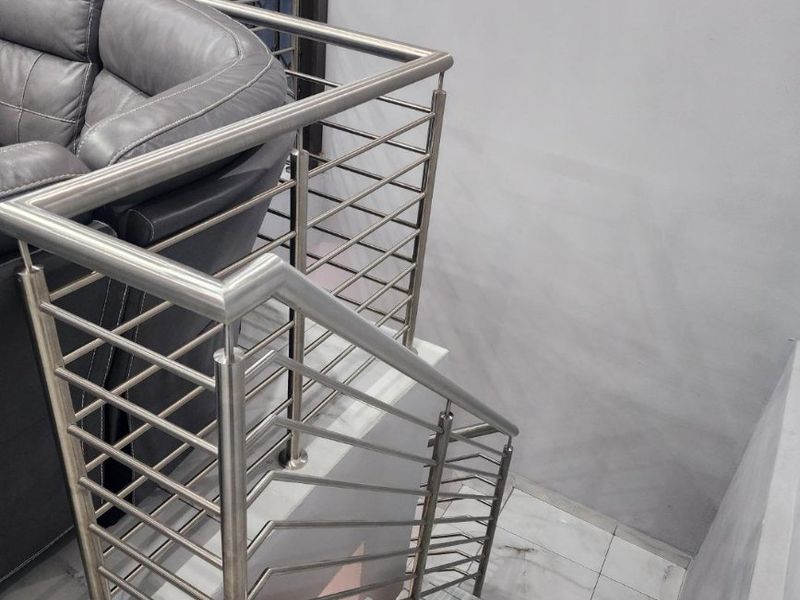 A modern staircase featuring a sleek stainless steel balustrade and light-toned tiled steps, providing a clean and contemporary transition between levels.