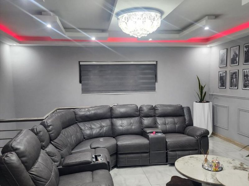 A modern living room featuring a recessed ceiling with integrated LED lighting, a central chandelier, and elegant wainscoting on the walls.