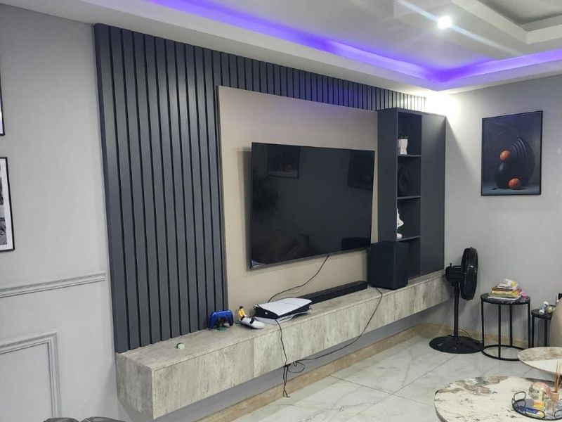 Modern living room featuring a custom built-in media wall with slatted paneling, integrated shelving, and ambient LED ceiling lighting.