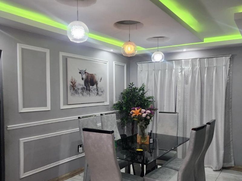 A modern dining room featuring decorative wainscoting, marble-look floor tiles, and a sophisticated recessed ceiling with integrated LED accent lighting and pendant fixtures.