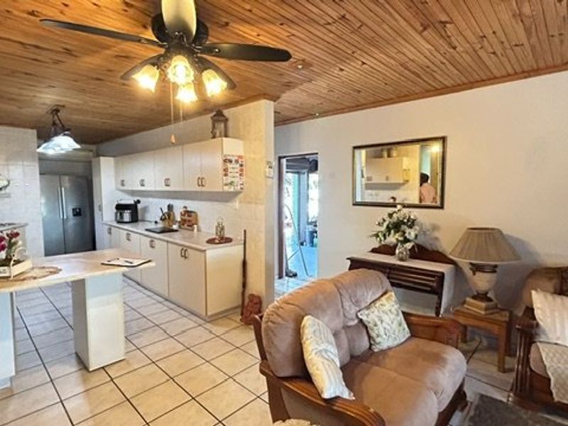 Open-plan living and kitchen area featuring a timber ceiling, tiled flooring, and functional built-in cabinetry with a central kitchen island.