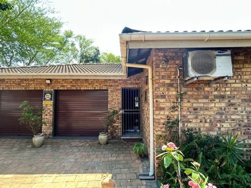 Front exterior view featuring a face-brick facade, double garage with roller shutter doors, paved driveway, and an installed air conditioning unit.