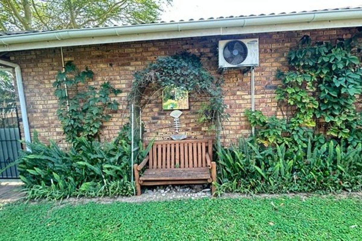 Rear exterior view of the property featuring a face brick wall, mounted air conditioning unit, and established garden area.