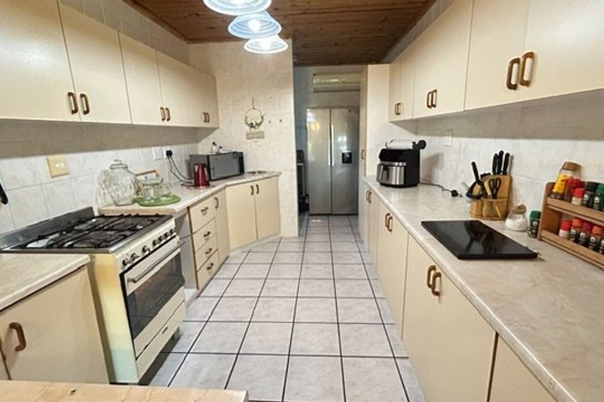 A functional galley-style kitchen featuring ample built-in cabinetry, gas stove, oven, and tiled flooring with a timber-paneled ceiling.