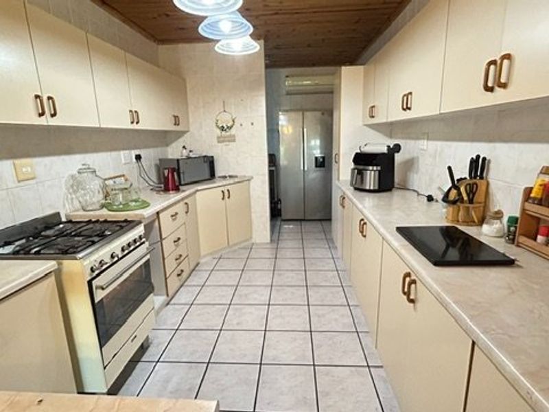 A functional galley-style kitchen featuring ample built-in cabinetry, gas stove, oven, and tiled flooring with a timber-paneled ceiling.