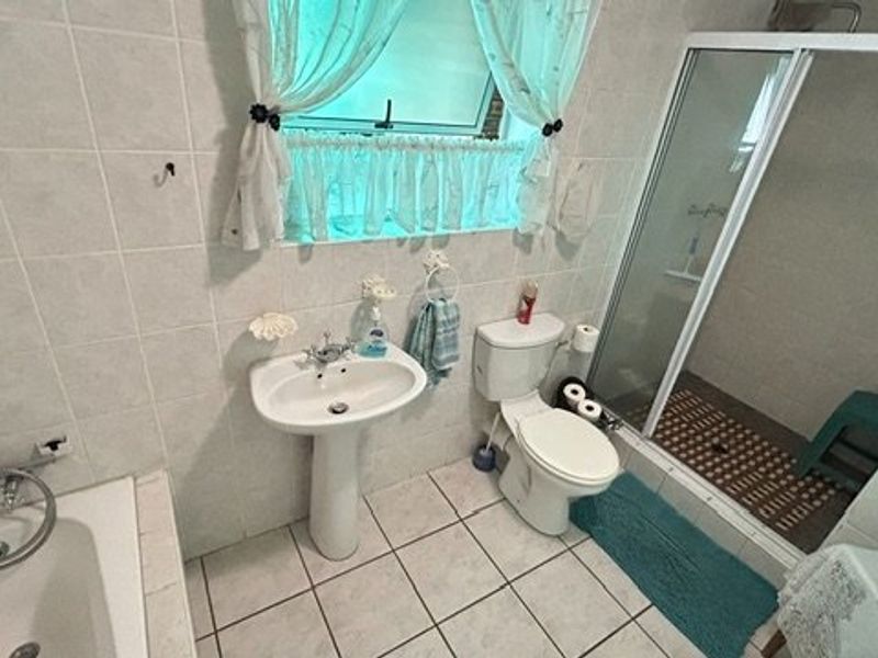 A functional bathroom featuring a pedestal basin, toilet, separate shower enclosure, and a bathtub with full-height wall tiling.