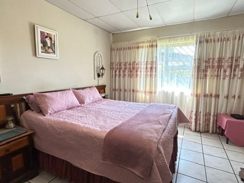 A bedroom featuring tiled flooring, security bars on the window, and a drop ceiling, offering a functional space with potential for cosmetic updates.