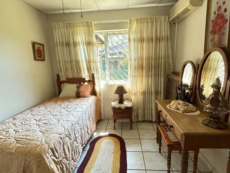 A functional bedroom featuring tiled flooring, a wall-mounted air conditioning unit, and a window fitted with security bars.
