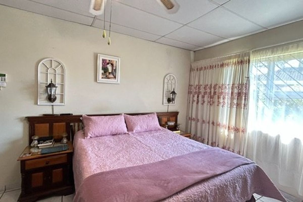 A functional bedroom featuring tiled flooring, a ceiling fan, and an integrated alarm system keypad.