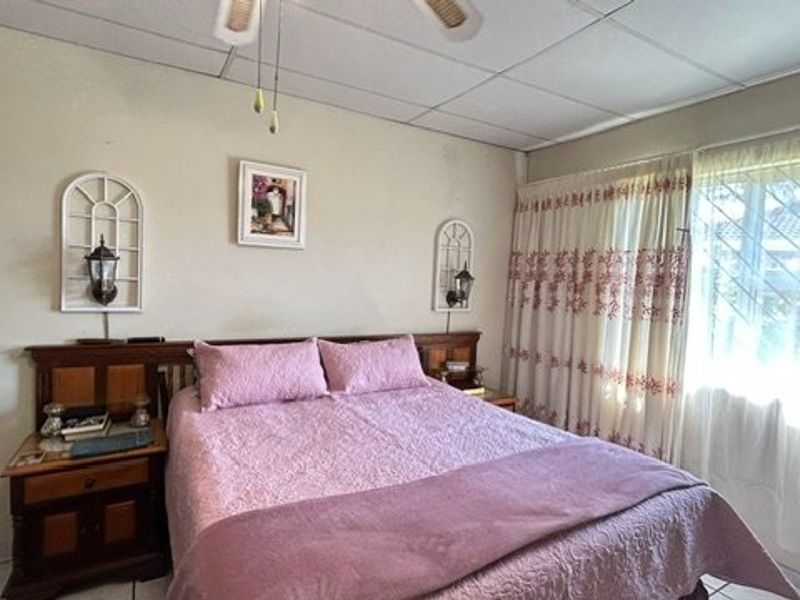 A functional bedroom featuring tiled flooring, a ceiling fan, and an integrated alarm system keypad.
